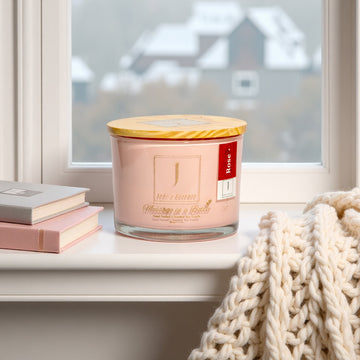 3_wick_eco_friendly_scented _candle_Rose Candle with a wooden lid on a windowsill with books and a blanket.