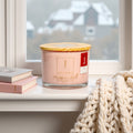 3_wick_eco_friendly_scented _candle_Rose Candle with a wooden lid on a windowsill with books and a blanket.
