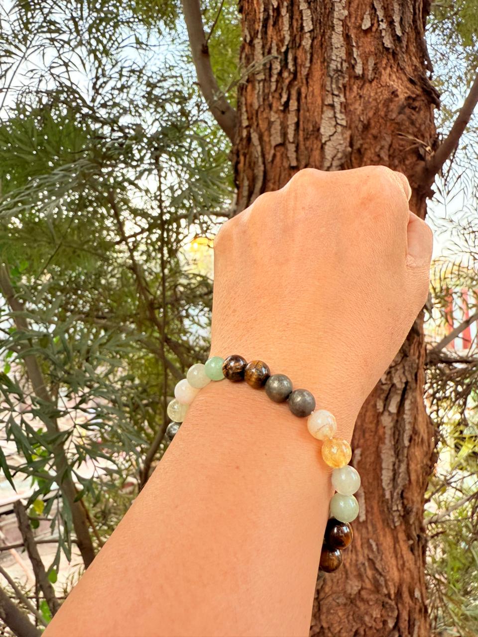 Hand wearing a beaded bracelet against a natural background with trees.