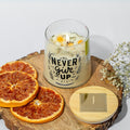 eco friendly Candle with 'Never Give Up' text on a wooden board with dried oranges and flowers.