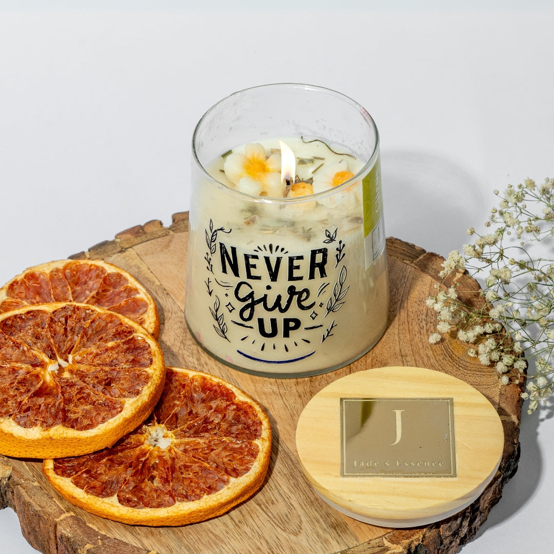 eco friendly Candle with 'Never Give Up' text on a wooden board with dried oranges and flowers.