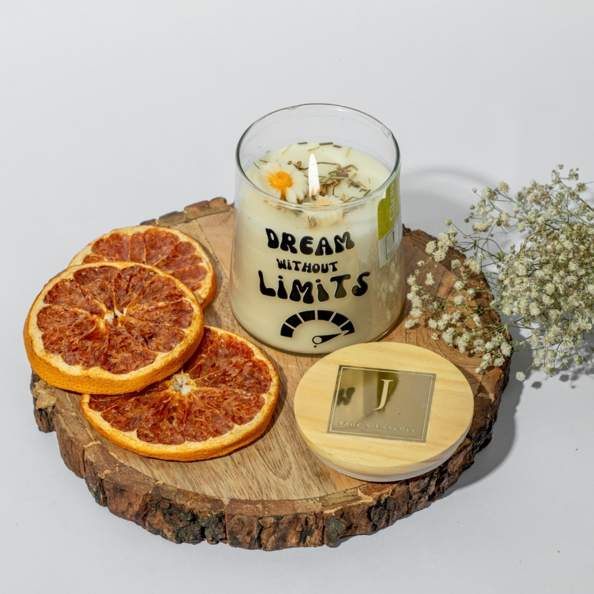 eco friendly Candle with 'Dream Without Limits' text on a wooden coaster with dried oranges and flowers.