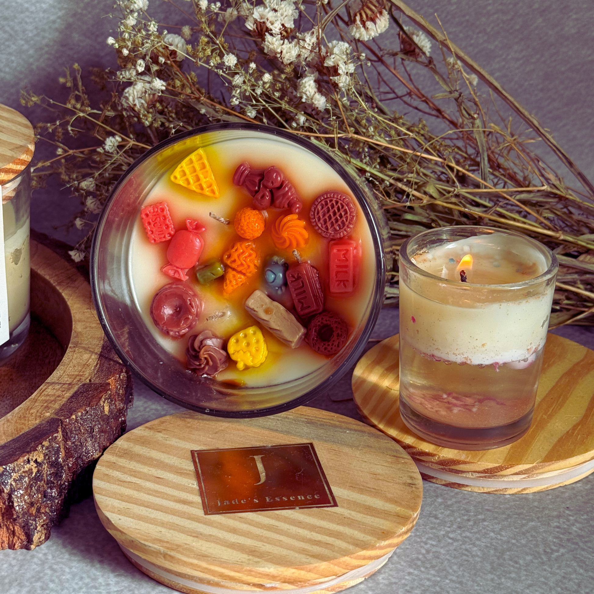 ecofriendly Candle with colorful candy pieces inside, surrounded by dried flowers and another candle on a wooden coaster.