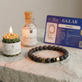 Beeswax candle, Epsom salt bottle, and bracelet on a stone surface with a GGLAB card in the background.