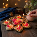 Candlelit diya with flowers on a wooden surface, blurred lights in the background
