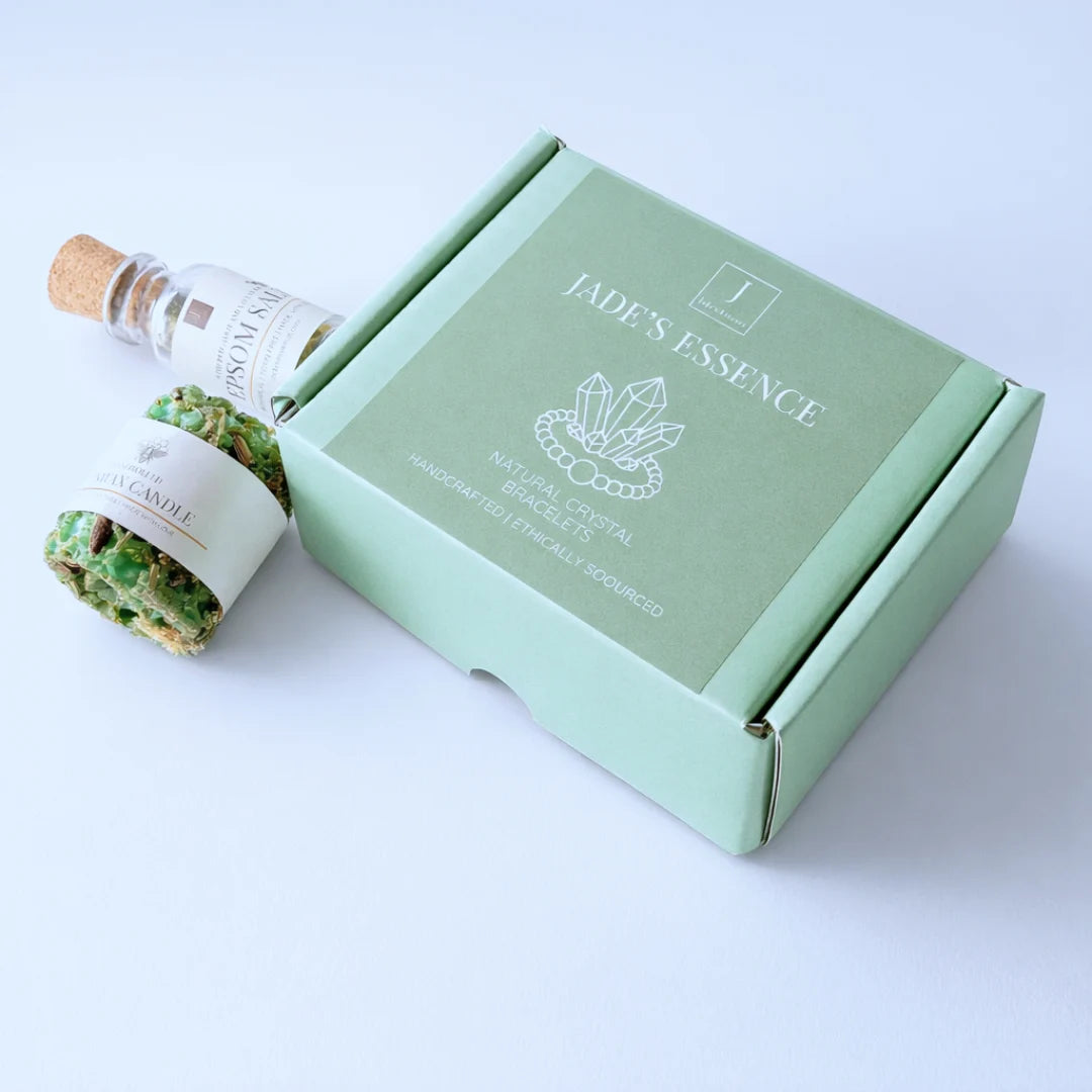 Two beaded bracelets on a wooden surface with a lit candle, bottle of Epsom salt, and GCLAB card in the background.