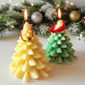 Two Christmas tree-shaped candles, one yellow and one green, with lit flames against a festive background.