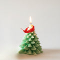 Christmas tree-shaped candle with a lit wick on a white background