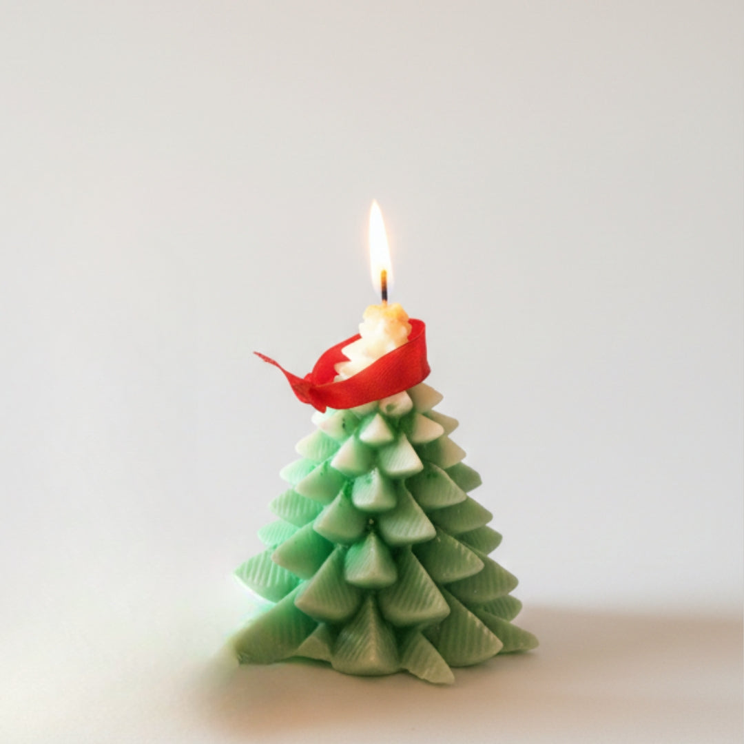 Christmas tree-shaped candle with a lit wick on a white background