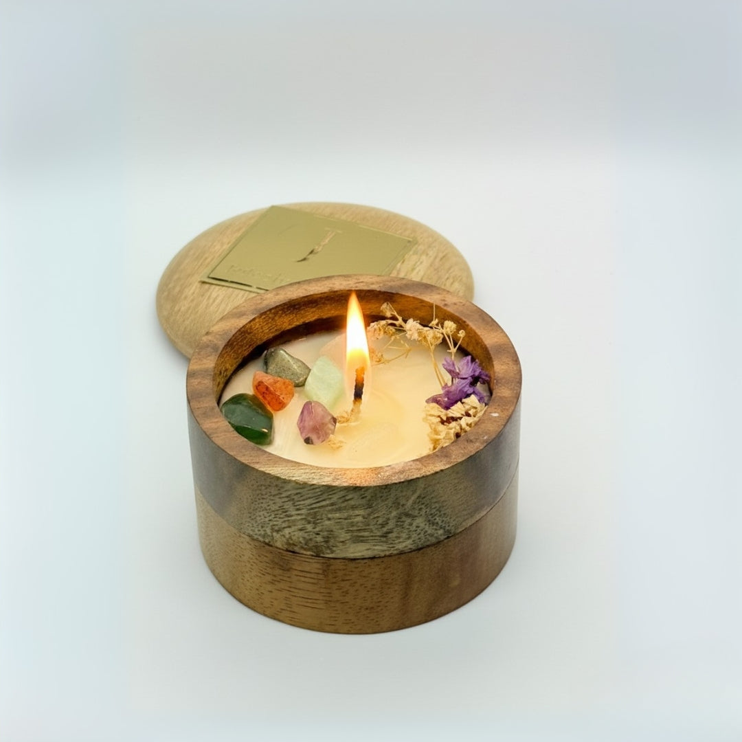 Wooden container with a lit candle inside, featuring small stones and flowers on a light background