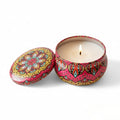Colorful patterned candle in a tin with a lit candle inside on a white background