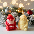 Two Santa Claus-shaped candles with a Christmas tree and ornaments in the background.