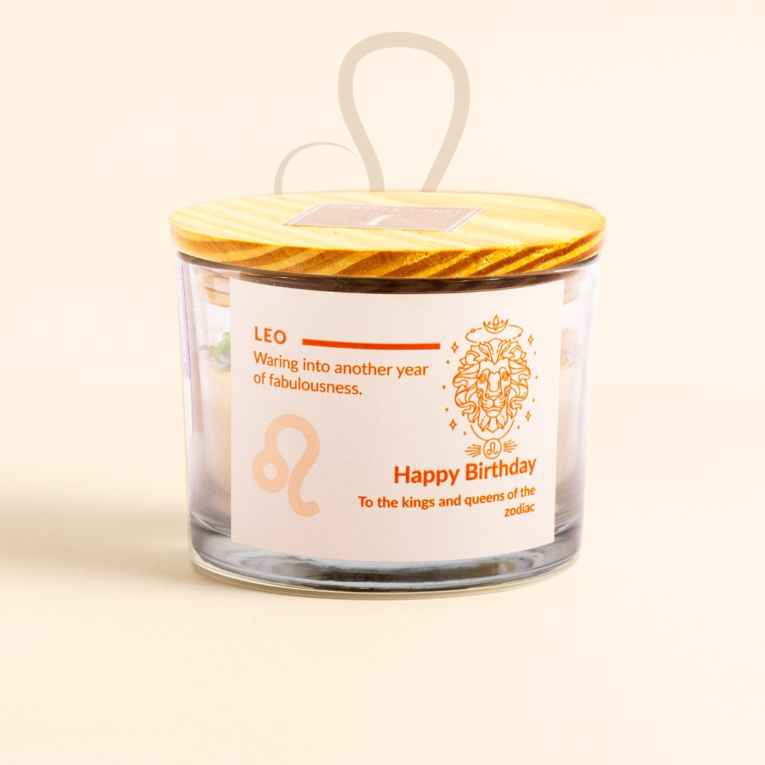 Glass candle with a yellow lid featuring a Leo zodiac design and birthday message on a beige background.